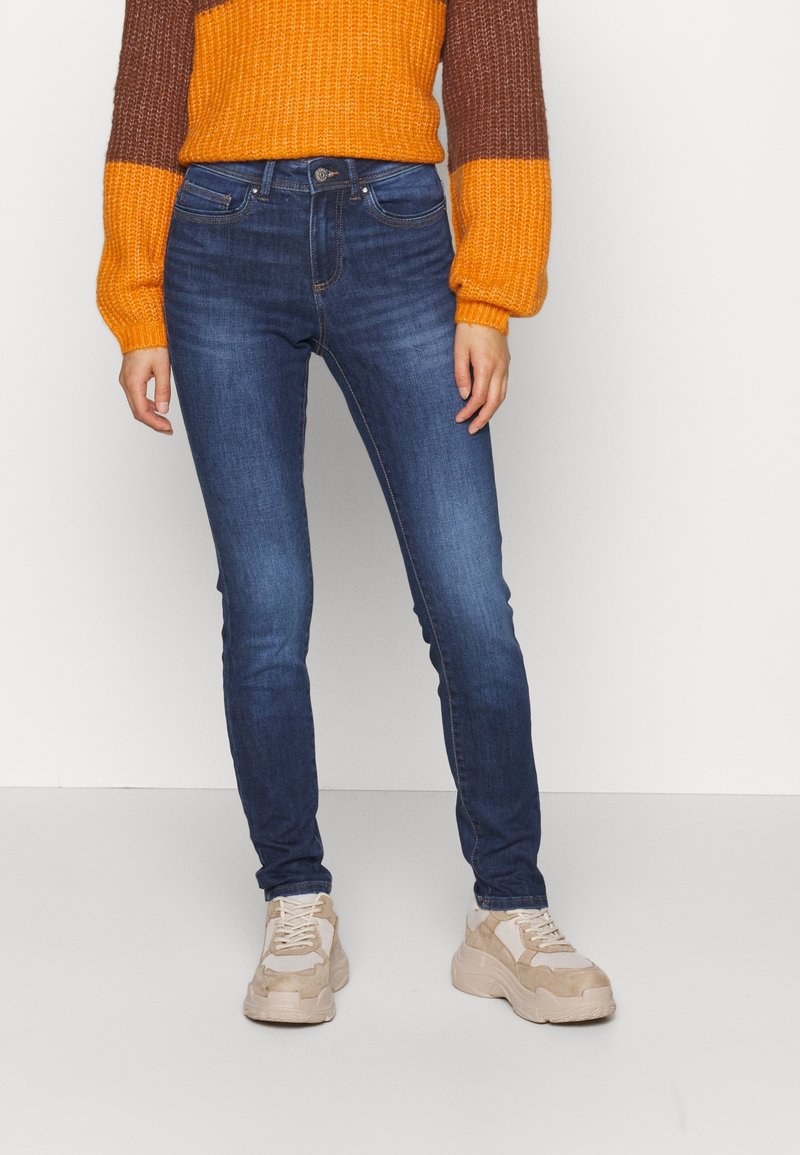 Tunna blåjeans med en slät denimtextur, visade tillsammans med en texturerad flerfärgad tröja och beige sneakers, som framhäver en avslappnad stil.