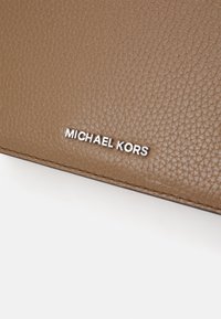 Portafoglio in pelle marrone con texture, caratterizzato dal logo bianco "MICHAEL KORS", con cuciture a contrasto lungo i bordi.