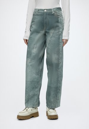 Person wearing loose-fitting, faded blue-green textured pants and white platform lace-up shoes with thick brown soles.