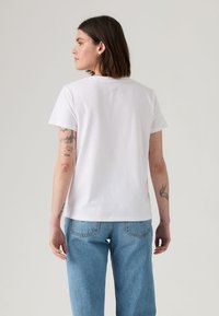 T-shirt branca de algodão com corte clássico, mangas curtas e decote redondo, combinada com jeans de ganga azul claro.