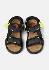 Mustat sandaalit säädettävillä remmeillä, joissa on purppuran ja neonkeltaisen väriset yksityiskohdat. Niissä on korkkipohja ja kumipohja.