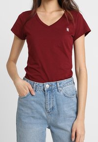 Röd V-ringad t-shirt i mjukt tyg, med korta ärmar och en liten logotyp. Matchad med ljusblå högmidjade jeans.