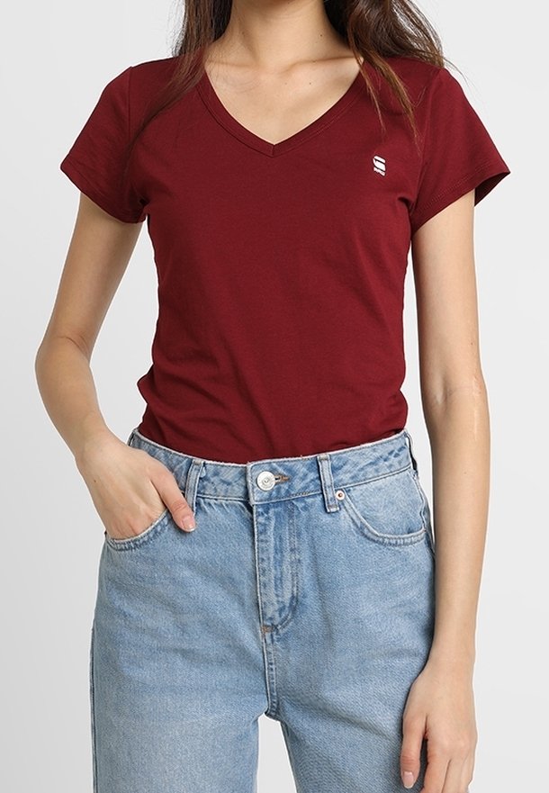Röd V-ringad t-shirt i mjukt tyg, med korta ärmar och en liten logotyp. Matchad med ljusblå högmidjade jeans.