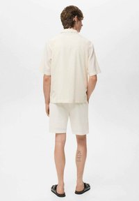 Chemise à manches courtes, beige clair, assortie à un short blanc texturé. L'ensemble présente une coupe décontractée et un design simple. Sandales noires portées.
