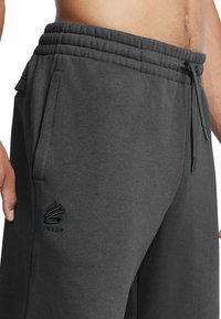 Pantalones de chándal gris oscuro, confeccionados con tejido suave, que cuentan con una cinturilla elástica con cordón ajustable y bolsillos laterales. Incluye un logo bordado en negro.