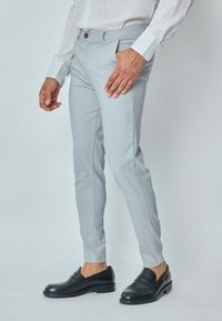 Pantalons gris clair ajustés en tissu lisse, présentant une coupe slim, un design minimaliste, des poches latérales et une fermeture à un bouton.
