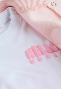Biely sveter s textúrovaným ružovým potlačou "HELLO", vrstvený pod mäkkou ružovou fleecovou bundou so zapínaním na gombíky a rebrovanými manžetami.
