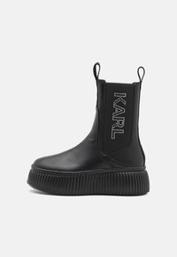 Bottes chelsea noires en cuir lisse avec des panneaux latéraux élastiques, une semelle plateforme striée, et ornées du nom "KARL" en strass.