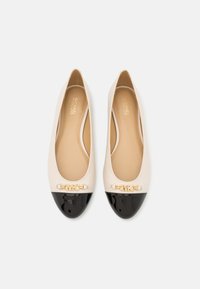 Ballet flats dengan bagian atas kulit beige yang halus, tutup jari hitam mengilap, dan perangkat keras logo emas di bagian depan. Pelapis dalam yang lembut.