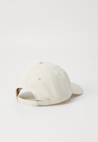 Casquette en coton beige avec une visière incurvée, sangle ajustable à l'arrière et trous de ventilation cousus. Design simple, sans motifs supplémentaires.
