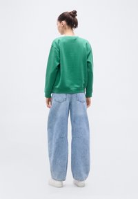 Sweat-shirt vert à col rond et poignets côtelés associé à un jean large bleu clair. Le tissu semble doux avec une coupe décontractée.