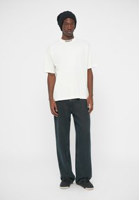 Biała bawełniana koszulka z okrągłym dekoltem, w połączeniu z luźnymi ciemnoniebieskimi jeansami. Dopełnieniem stroju jest granatowa dzianinowa czapka.