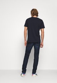 Granatowa bawełniana koszulka z krótkim rękawem, w połączeniu z ciemnoniebieskimi dżinsami i białymi trampkami z niebieskimi i czerwonymi akcentami.