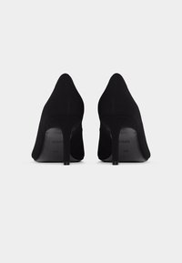 Μαύρα σουέντ ψηλοτάκουνα παπούτσια, φωτογραφημένα από πίσω πάνω σε λευκό φόντο, μέγεθος 40, με μυτερές γόβες και λεπτή σιλουέτα.