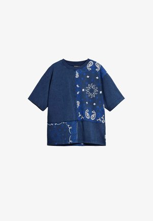 Camiseta de mezclilla azul con mangas cortas, que presenta patrones de paisley y flores en blanco y azul claro en el lado delantero izquierdo.