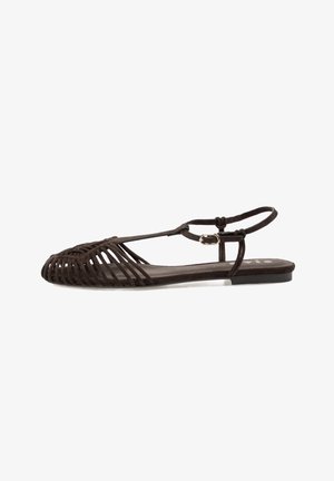 Sandalia plana de color marrón oscuro con tiras entrelazadas, hebilla en el tobillo y punta abierta, diseñada para uso casual.