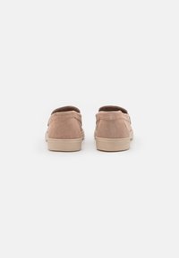 Un paio di scarpe slip-on in suede beige viste dal retro, posizionate affiancate su uno sfondo bianco semplice.