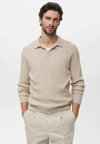 Suéter de punto acanalado beige con cuello y mangas largas, combinado con pantalones de color claro. Textura suave y un ajuste casual.