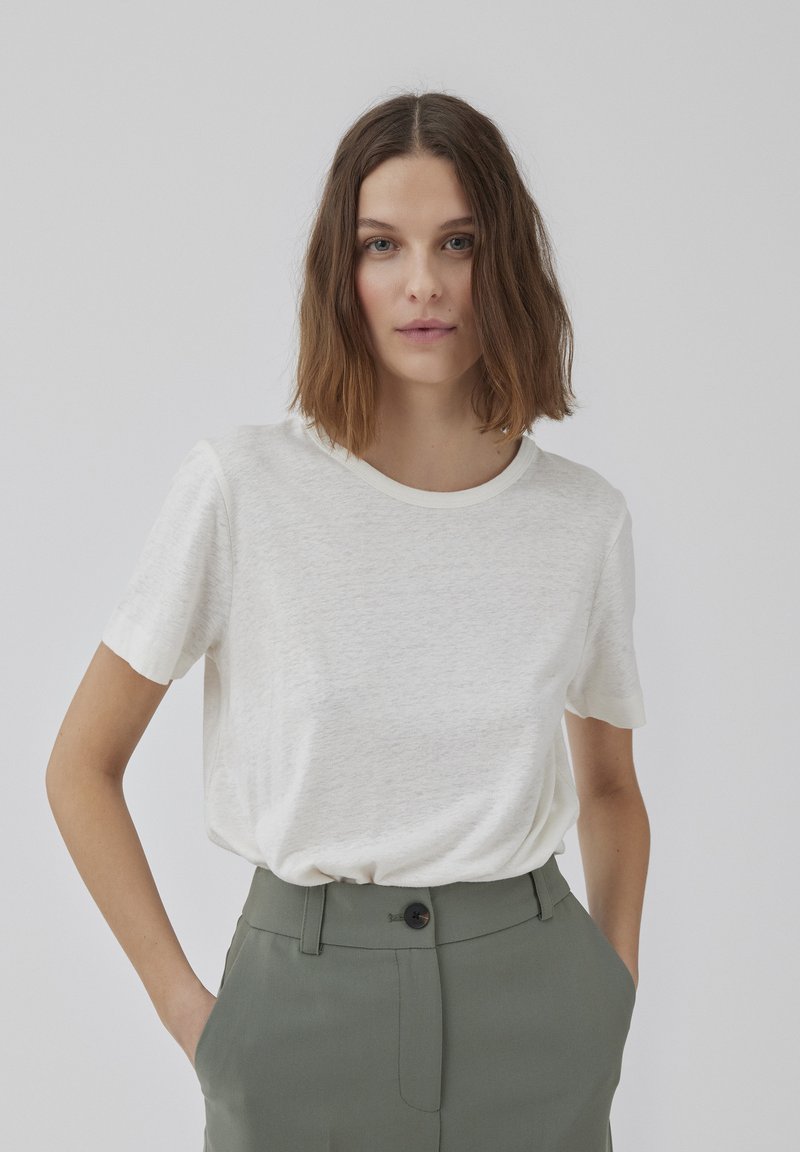 Hvid kortærmet t-shirt med rund halsudskæring, lavet af et struktureret stof, parret med olivengrønne skræddersyede bukser.