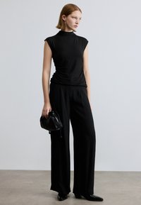 Top negro justo com decote alto, combinado com calças pretas de perna larga e uma pequena mala preta texturada. Tecido liso e elegante.