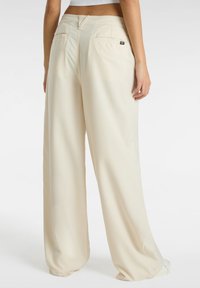 Pantaloni a gamba larga color crema realizzati in tessuto morbido, dotati di due tasche posteriori e un piccolo etichetta con il logo del brand sulla vita.