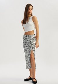 Witte crop top van textuurstof, gecombineerd met een lange rok met zwart-wit bloemenpatroon, voorzien van een zijsplit en een gladde textuur.