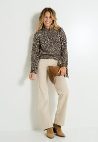 Blouse imprimée léopard à manches longues, pantalons beiges évasés et pochette frangée brune. Porté avec des bottines beige.