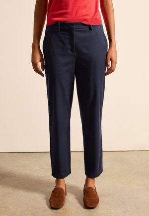 Navyblauwe op maat gemaakte broek met rechte pijpen, met plooien, zijzakken en een zachte textuur; gedragen met bruine suède schoenen.