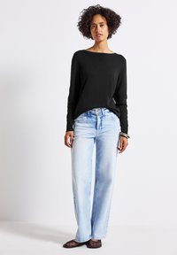 Svart långärmad tröja, ljusblå vida jeans och mesh-sneakers. Jeanssen har en urtvättad look och en fyrknapps gylf.