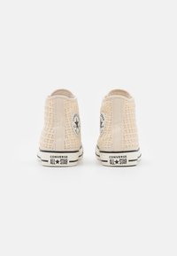 Beżowe sneakersy za kostkę z teksturowaną siateczkową cholewką, czarnymi akcentami i okrągłą naszywką z logo. Gumowe podeszwy z kontrastowymi paskami.