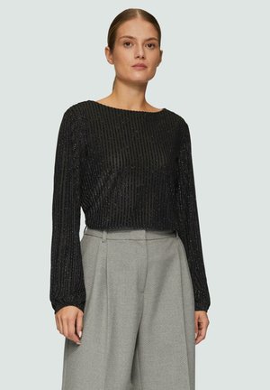 Haut noir à manches longues avec des rayures verticales texturées et une coupe courte. Associé à un pantalon large taille haute de couleur gris clair.