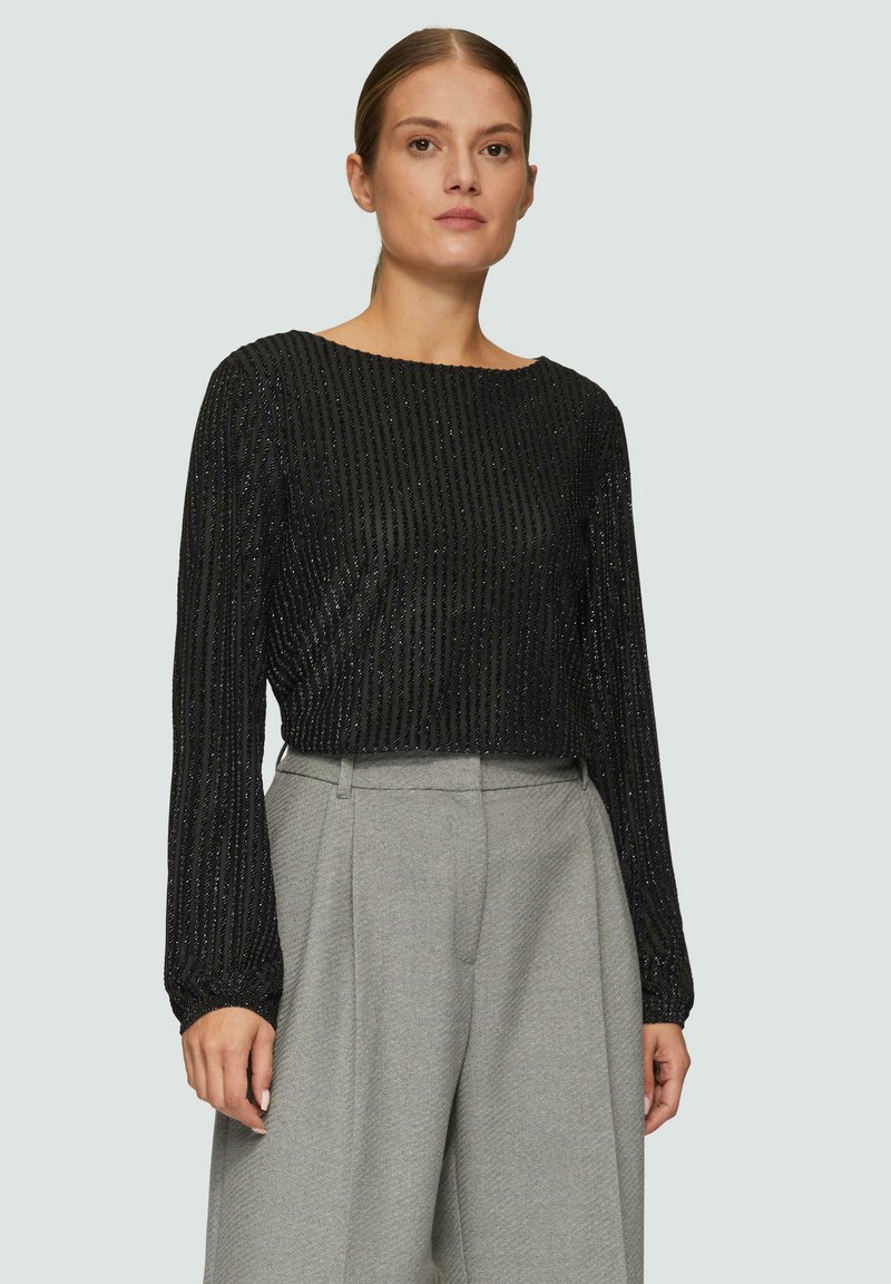Schwarzes, langärmliges Oberteil mit strukturierten vertikalen Streifen und einem cropped Design. Kombiniert mit hellgrauen, hochgeschnittenen, weit geschnittenen Hosen.