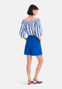 Blaue schulterfreie gestreifte Bluse mit Puffärmeln, kombiniert mit knielangen blauen Shorts und blauen Sandalen mit Riemchen. Glatte Stoffoberfläche.