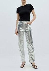 Zwart geribbeld top met korte mouwen gecombineerd met metallic zilveren hoge taille broek. De broek heeft een gladde, glanzende textuur en zijzakken.
