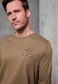 Hnědé dlouhé tričko s potiskem na hrudi. Měkká tkanina s volným střihem a kulatým výstřihem.