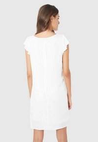 Vestido blanco hasta la rodilla con mangas cortas con volantes y un detalle de cremallera en la parte posterior. Tela suave con una textura lisa y un diseño sencillo.