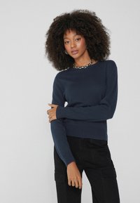Marineblauer, langärmliger Strickpullover mit Rundhalsausschnitt, gerippten Bündchen und Saum. Kombiniert mit schwarzen Cargo-Hosen, die eine schlanke Passform zeigen.