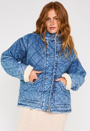 Veste en denim matelassé bleu clair avec des poignets en polaire crème douce. Elle est dotée de boutons-pression et de deux poches latérales. Finition texturée.