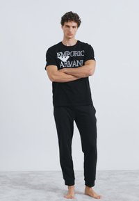 Čierne bavlnené tričko s bielym logom "Emporio Armani" v kombinácii s čiernymi teplákovými nohavicami. Jednoduchý dizajn, okrúhly výstrih, voľný strih.