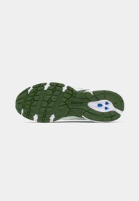 Semelle de chaussure New Balance verte avec motif de grip texturé et accents blancs et bleus sur un fond clair uni.