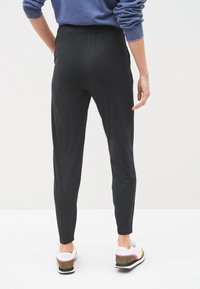 Black elastic waist pants with a tapered leg design. Smooth texture, featuring a simple cut, paired with white and colorful sneakers.