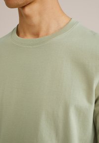 Šviesiai žalia trumparankovė marškinėlė, pagaminta iš švelnios medvilnės, su paprastu apvaliu kaklu ir lygiu paviršiumi, beveik be siuvimo detalių.