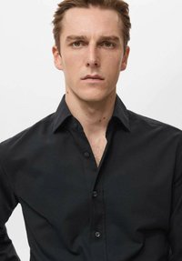 Czarna koszula zapinana na guziki z klasycznym kołnierzykiem, wykonana z gładkiego materiału. Charakteryzuje się dopasowanym krojem i subtelnym połyskiem. Bez wyraźnych wzorów.