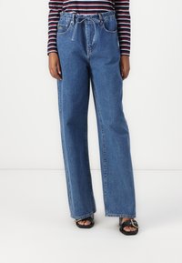 Lett blå, vide denimjeans med høy midje, frontlommer og et knytebelte-detalj. Har merkbare nagler og sømmer.
