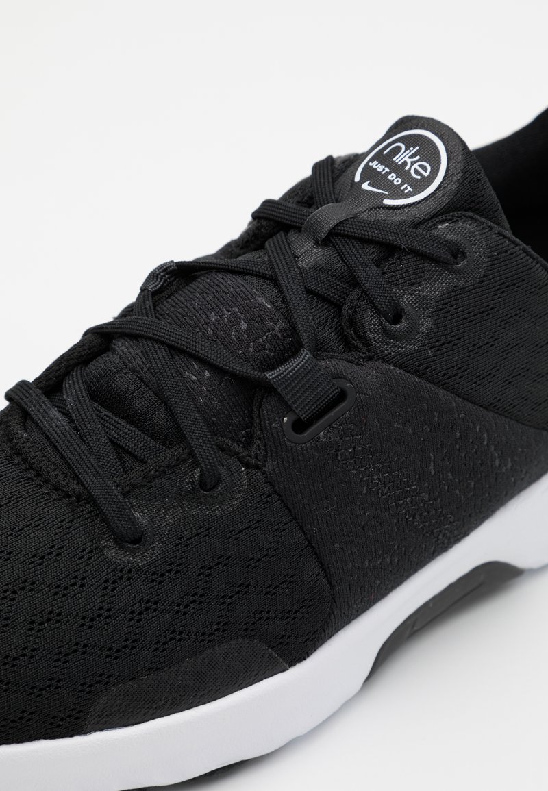 Zapato deportivo negro con parte superior de tejido texturizado, cierre de cordones y suela blanca. Incluye un logotipo circular en la lengüeta.