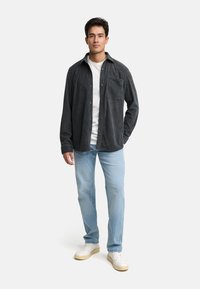 Camisa de franela de botones en gris oscuro, combinada con jeans azul claro. Camiseta blanca debajo. Zapatillas blancas con suelas marrones. Diseño simple.