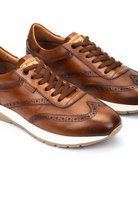 Bruine leren vetersneakers met gestructureerde accenten, brogue-details en een gevoerde zool. Merkenlogo op de tong; combinatie van tan en crème.