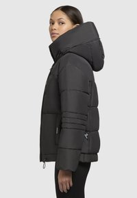 Giacca a vento nera con un grande cappuccio, design trapuntato e tasche con zip visibili. Presenta polsini elasticizzati e un orlo regolato.
