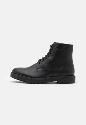 Bottines noires en cuir avec une finition lisse, bout rond, fermeture à lacets sur le devant et semelle en caoutchouc robuste. Design minimaliste avec des coutures ton sur ton.