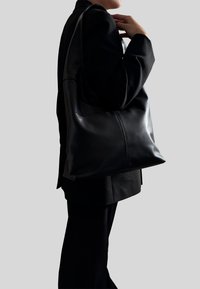 Czarna skórzana torba na ramię o miękkiej fakturze, minimalistycznym designie i solidnych rączkach; posiada przeszycie dla dodatkowej struktury.